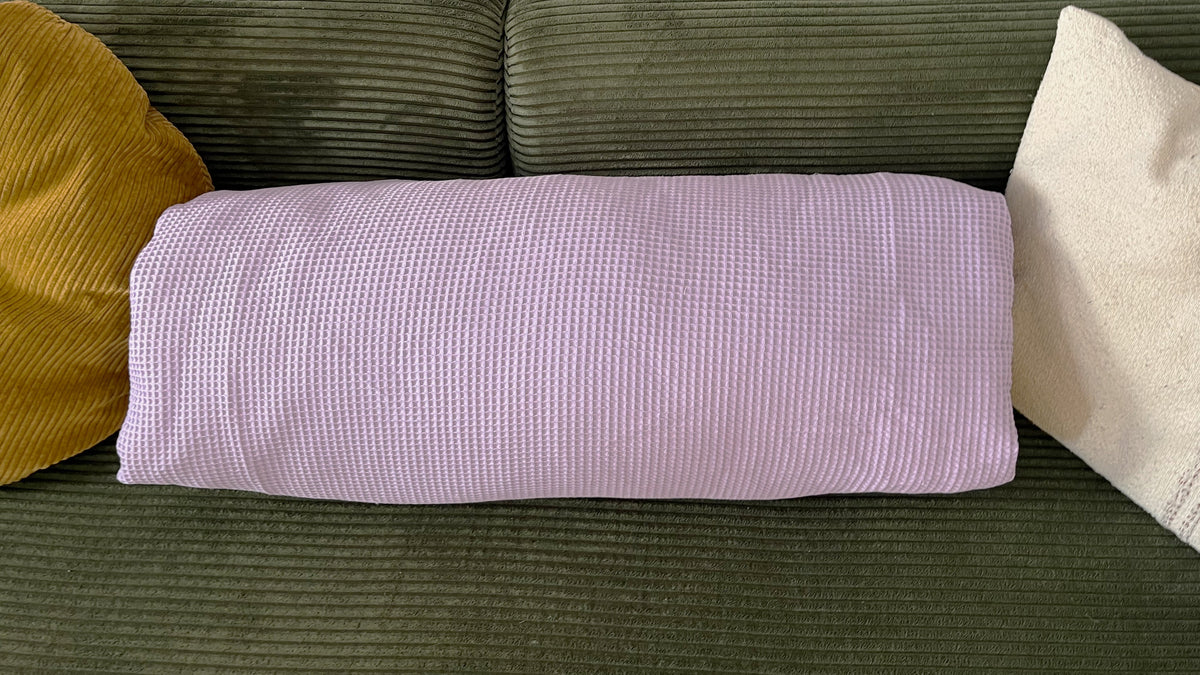 Die zusammengelegte Kissenjacke liegt als flaches Kissen zwischen zwei anderen Kissen auf einem grünen Sofa.